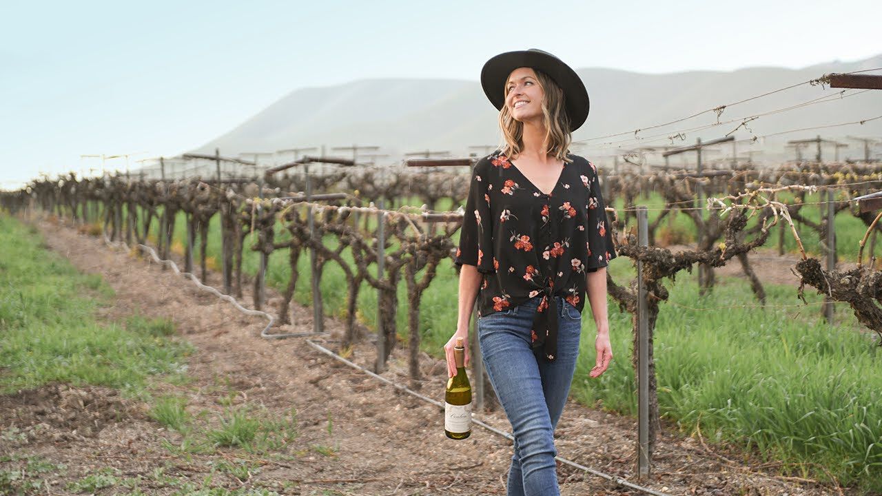 Woman walking in vineyard holding bottle of Cambria wine.